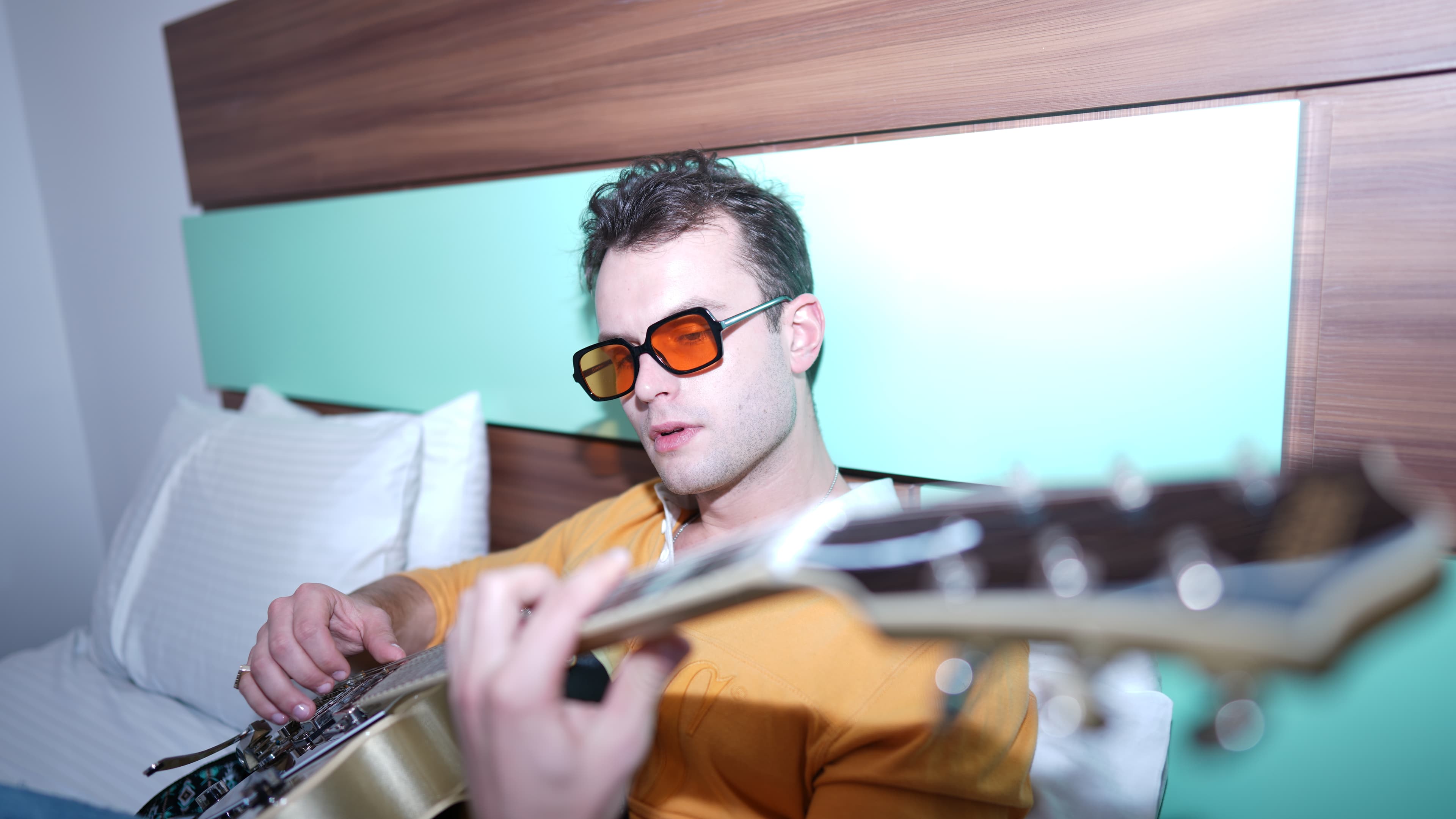 Sébastien Graux playing guitar on a hotel bed — the kind of session where a $99 guitar and an iPhone became a Ricky Martin placement